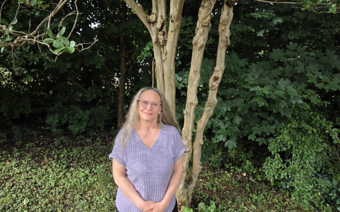 Peatra, wearing casual clothing, stand outside in front of a tree.
