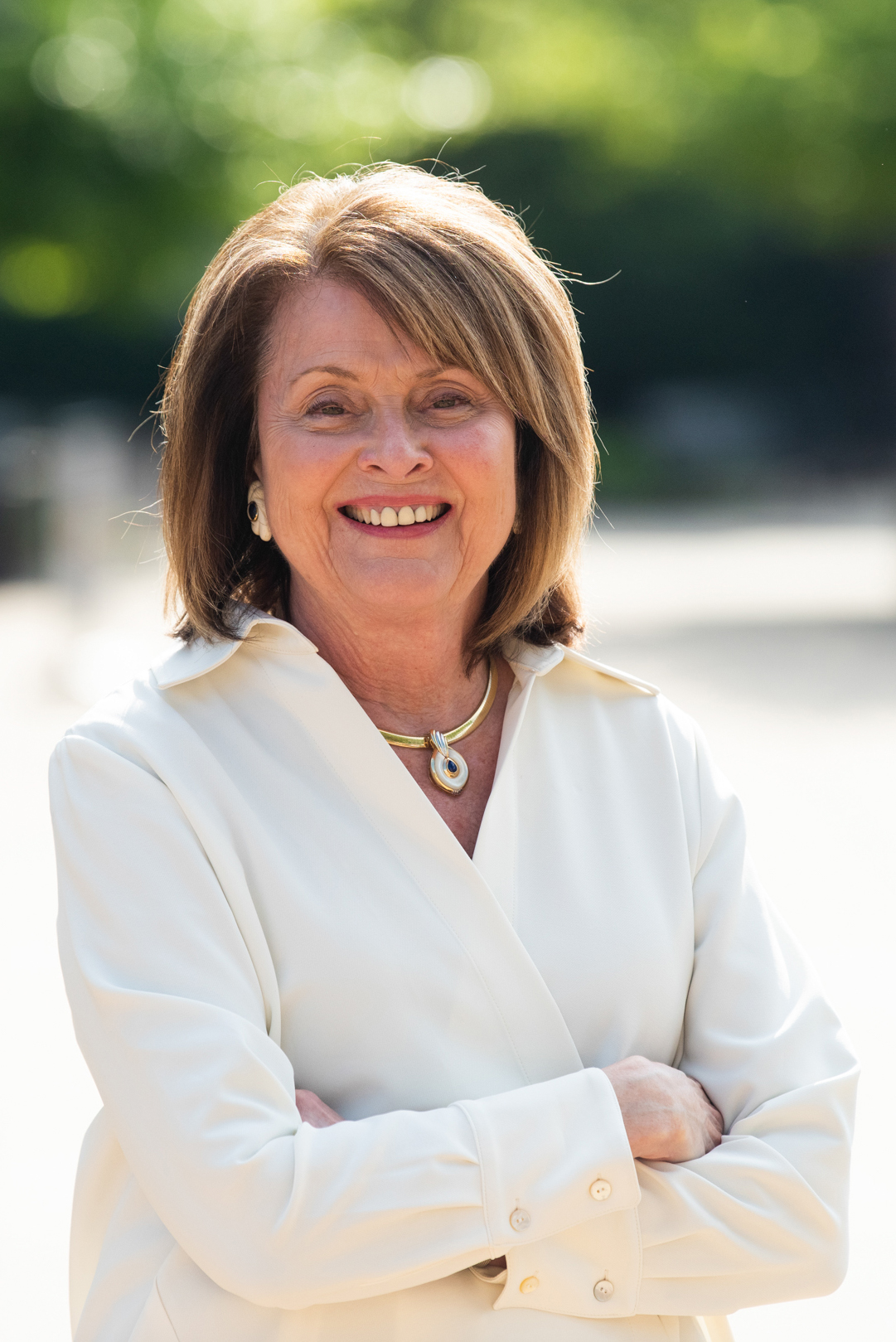 Dr. Carol Spalding smiles in an outdoor setting, she  is wearing cream colored business attire and jewelry.